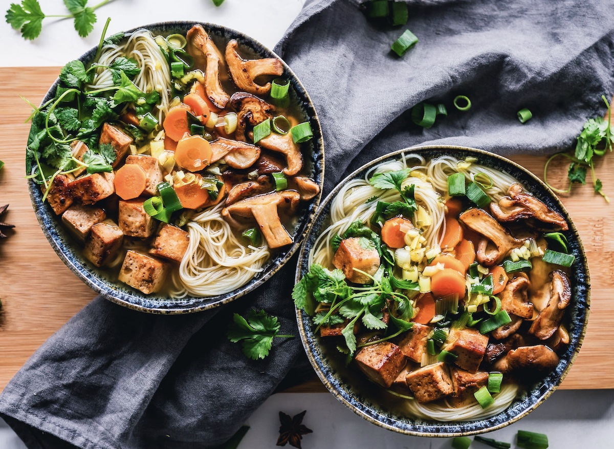 Two vegetable soups in bowls on cutting board with herbs and mushrooms
