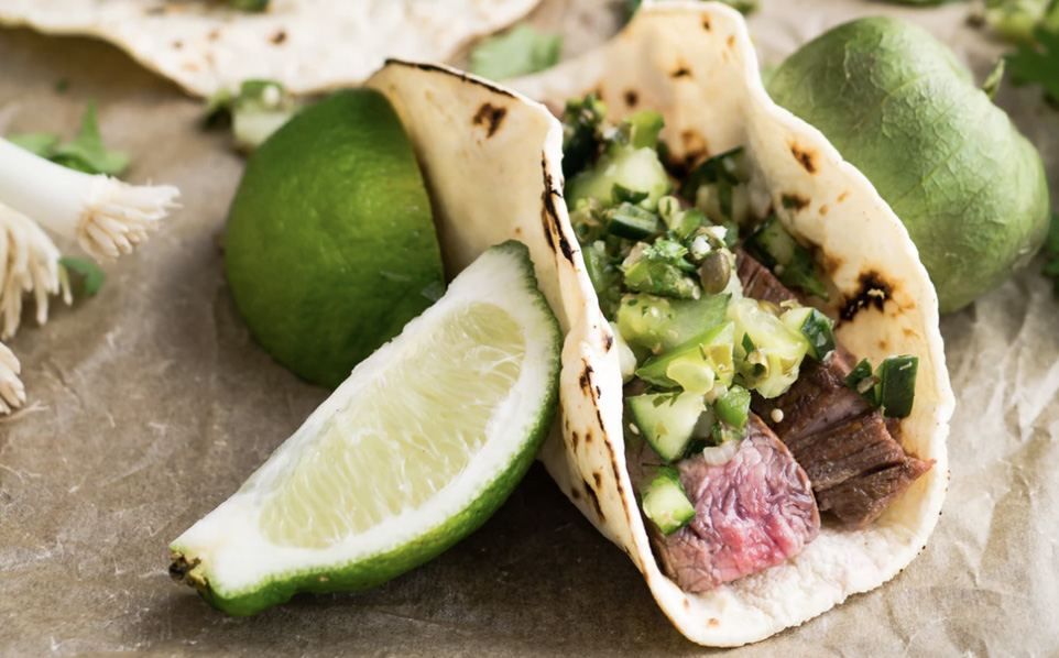 Taco on a table (meat and avocado inside), and some lime