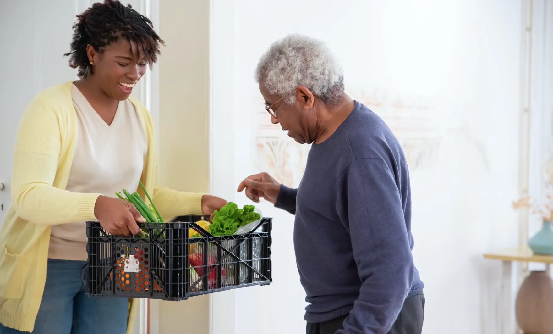 Woman holds a basket full of vegetables. A man picking some from the basket.