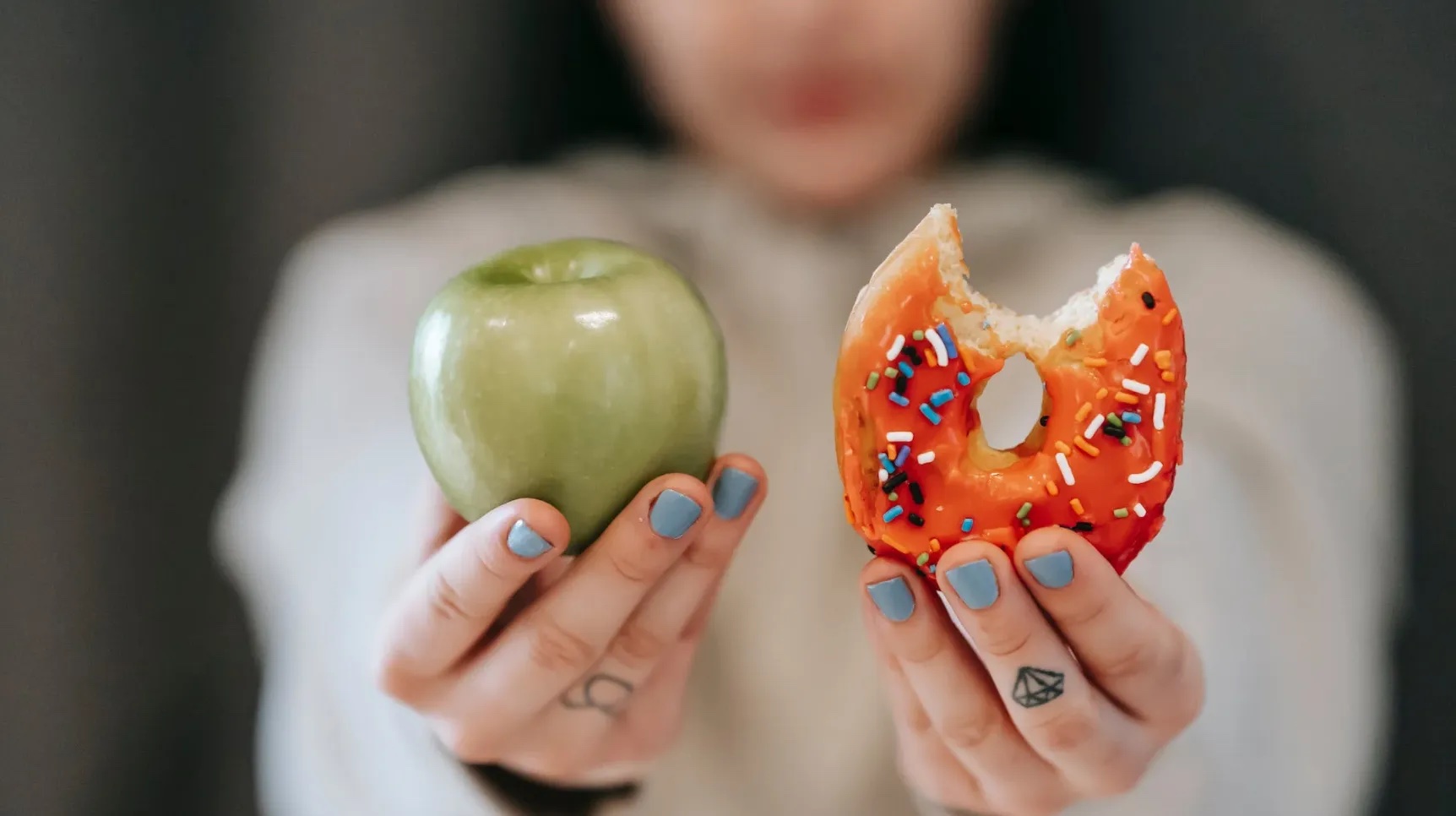 Someone is holding an apple in one hand and a donught in the other hand. Image: Pexels - Andres Ayrton