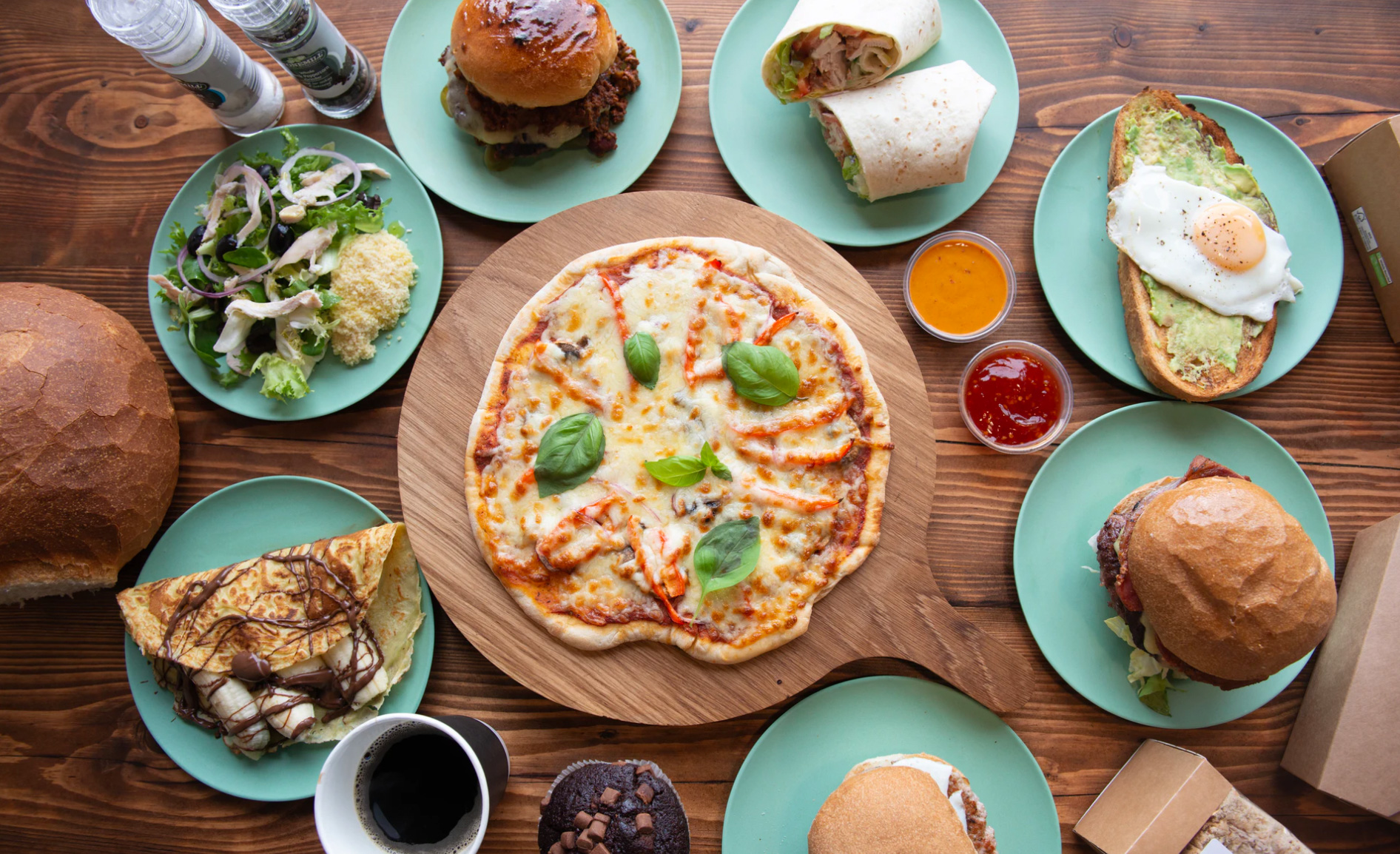 A table with many food selections of pizza, crepes, avocado toast, burgers 