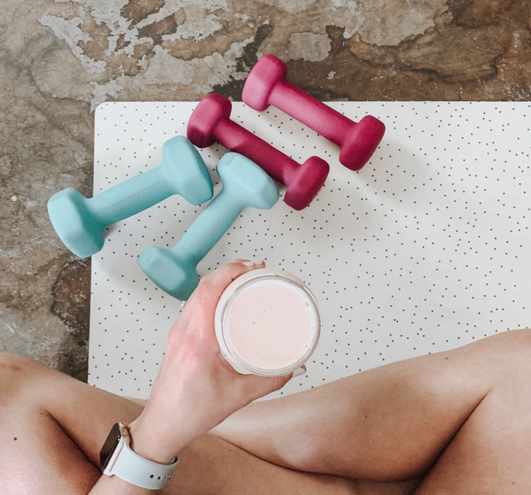 Woman drinking protein smoothie with weights at home