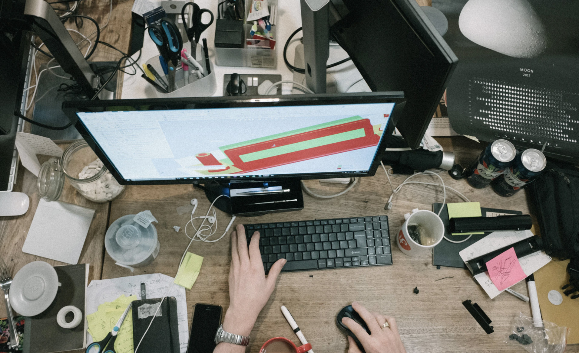 A woman that is busy in front of a computer with things surrounding her. 