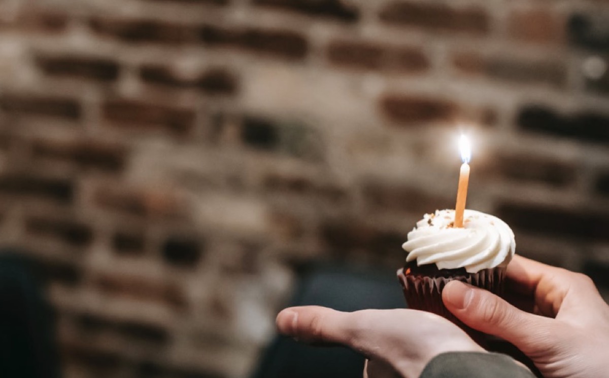 Individual holding cupcake with candle.