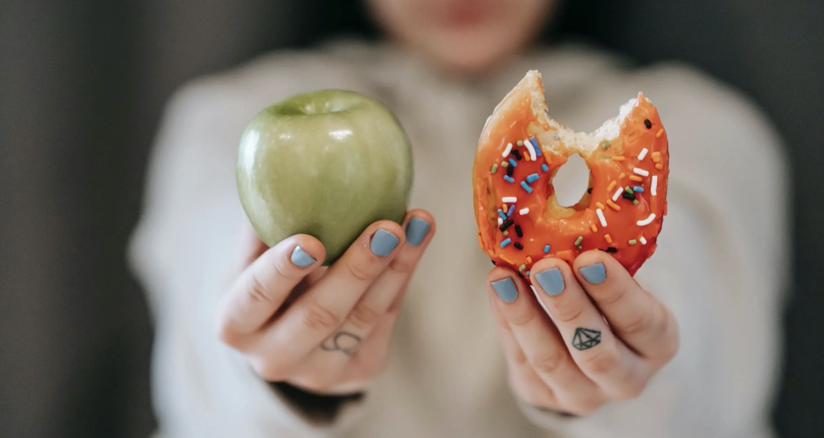 Woman holding an apple and a donut in each hand. 