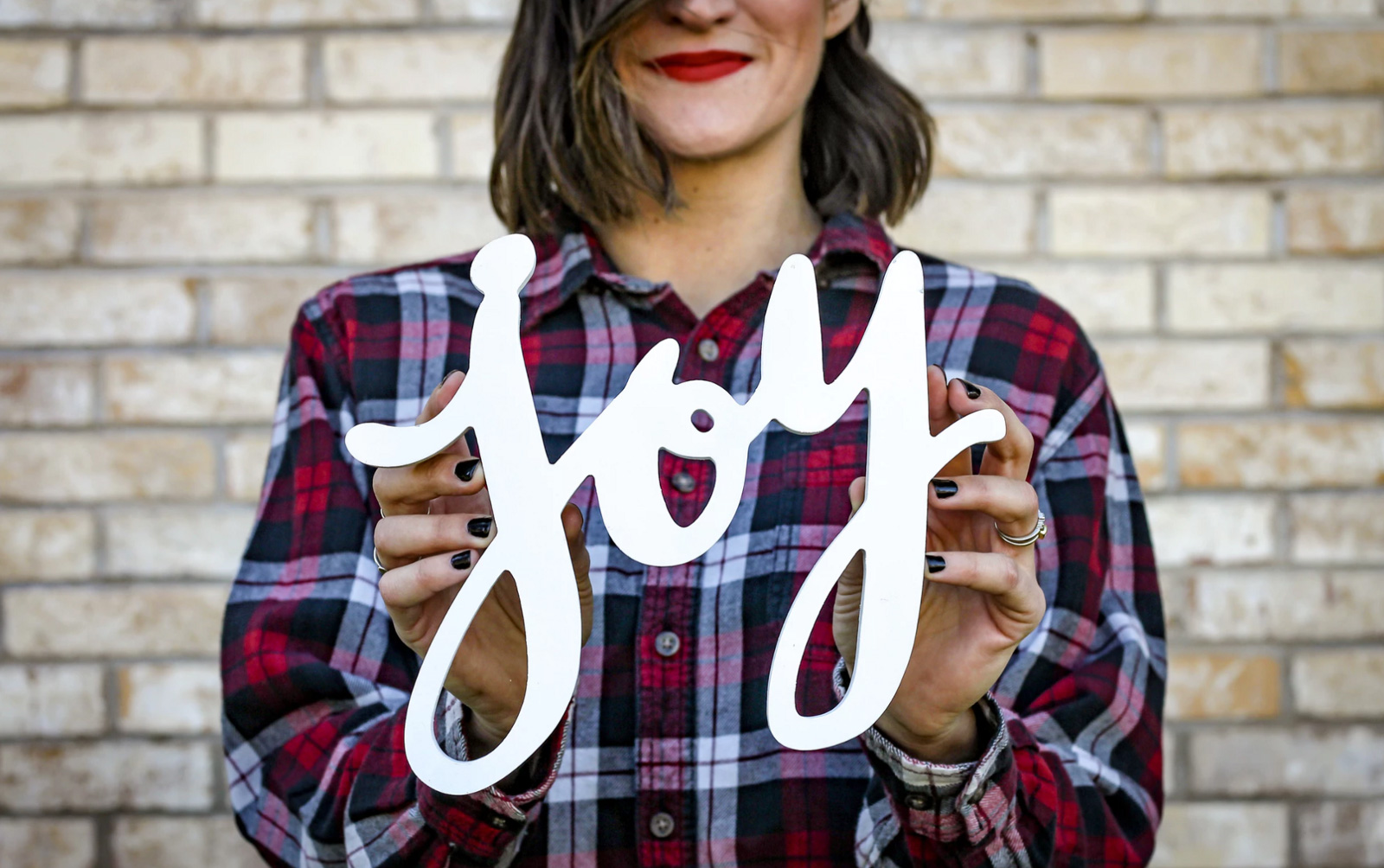 A woman smiling and holding up the word joy