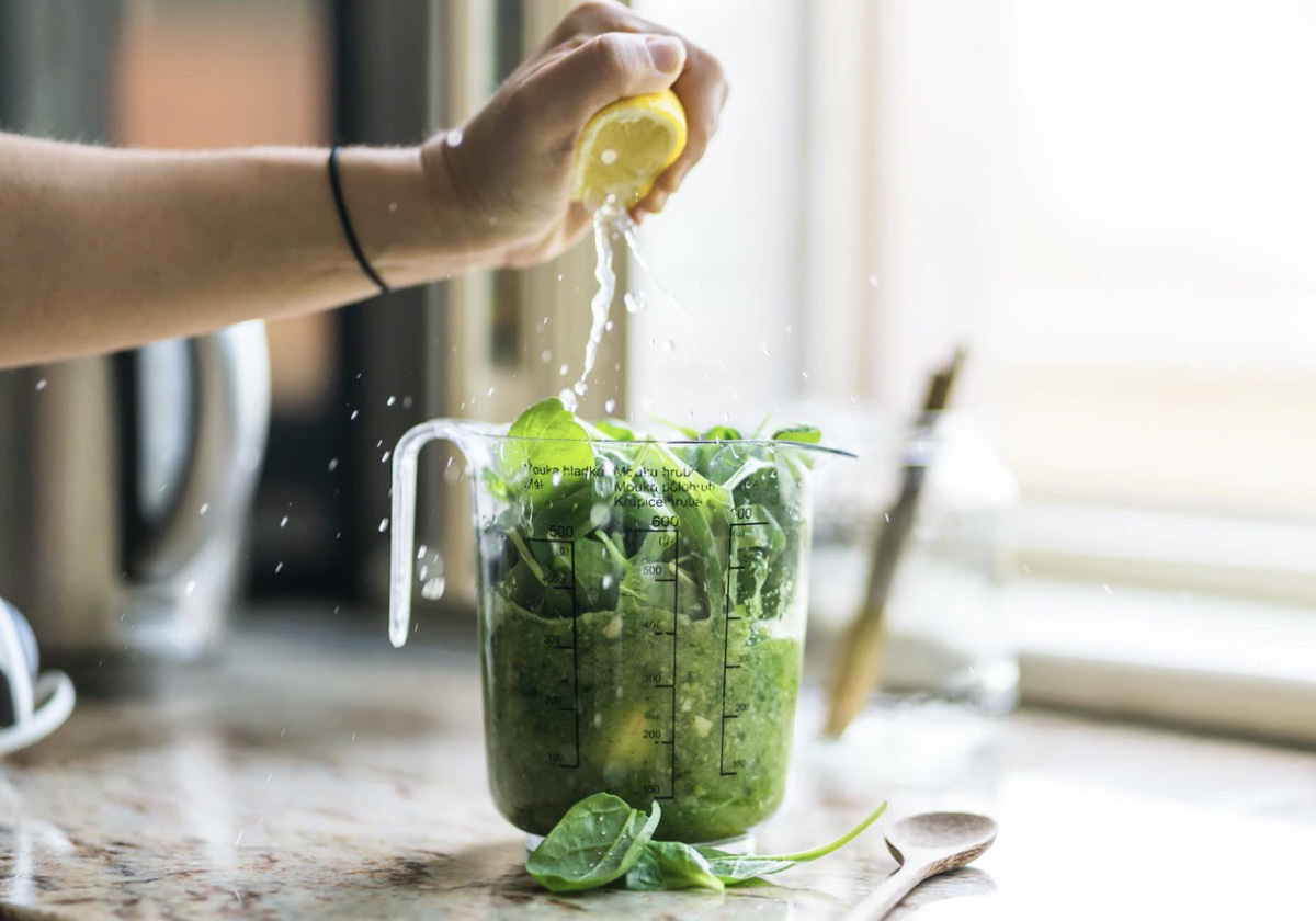 Individual squeezing lemon into a pitcher of greens. Unsplash - Jan Sedivy