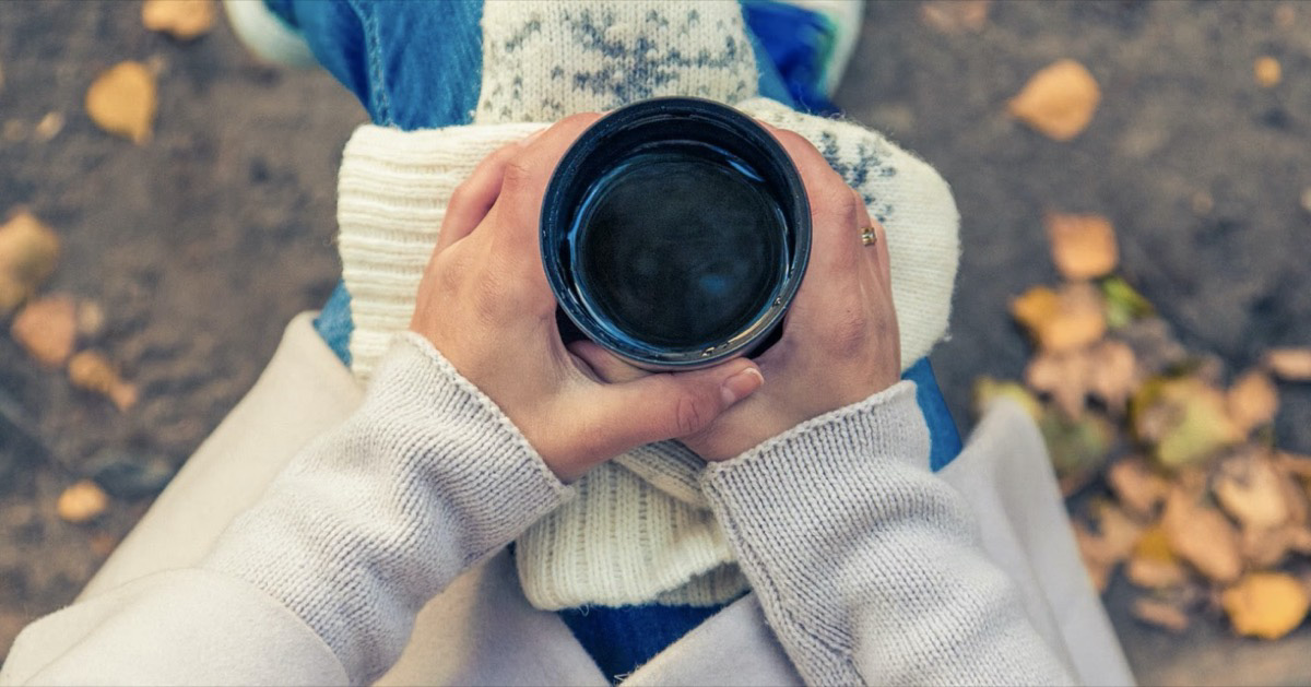 Woman sitting outside with a cup of coffee during the fall. 