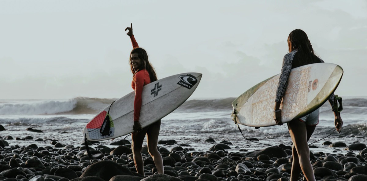 Two women going out to surf in the ocean. 