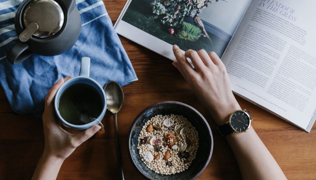 Individual having a cup of tea, reading and a bowl of oats for morning routine. 