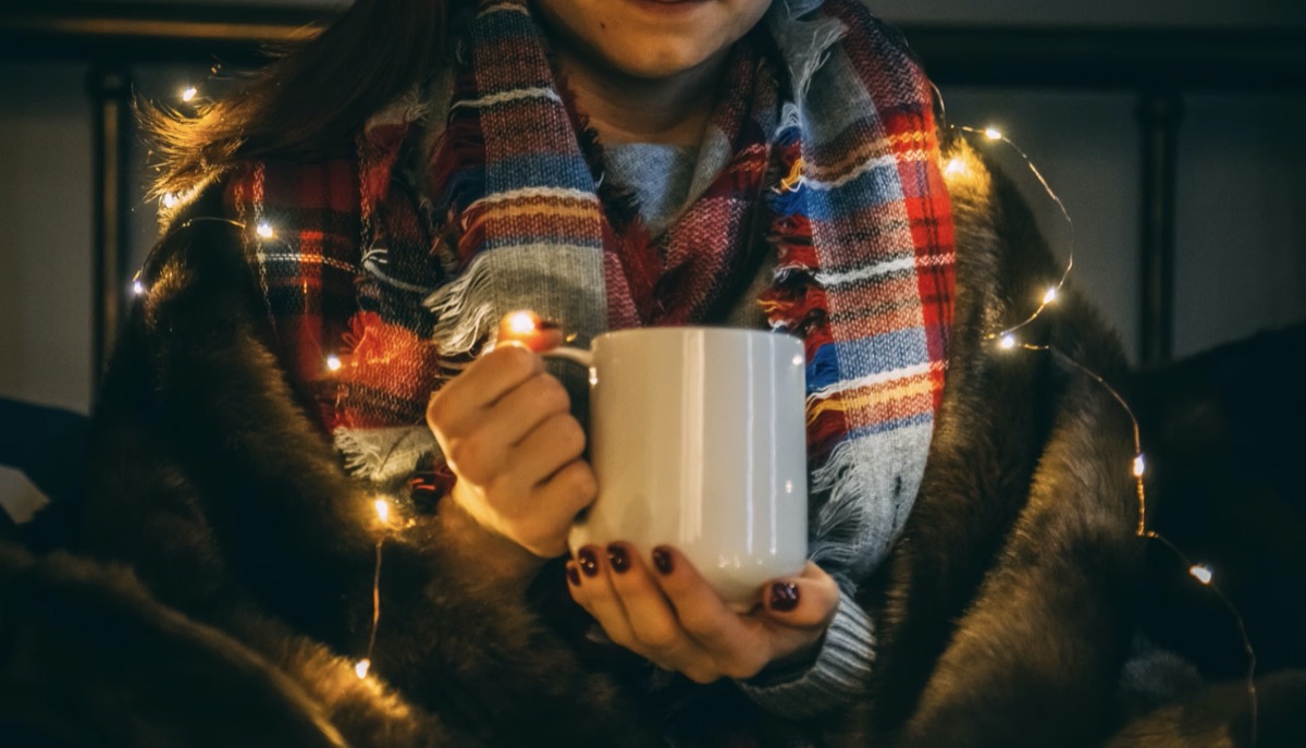 Woman holding mug with scarf and holiday lights. Unsplash - Alora Griffiths