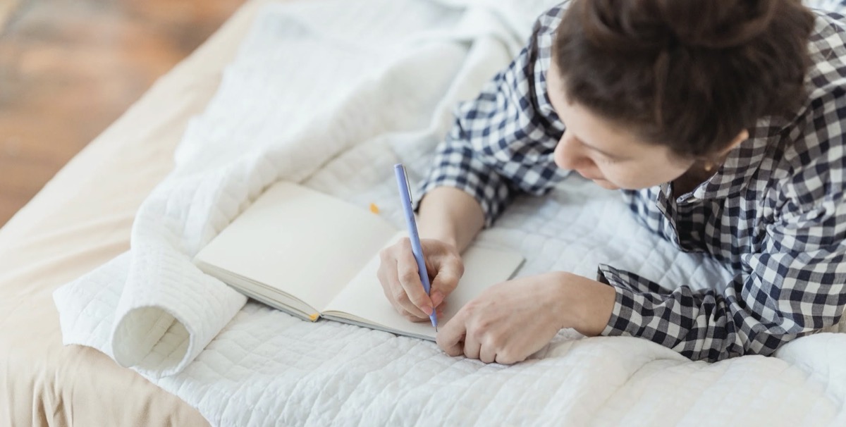 Woman laying on bed journaling 