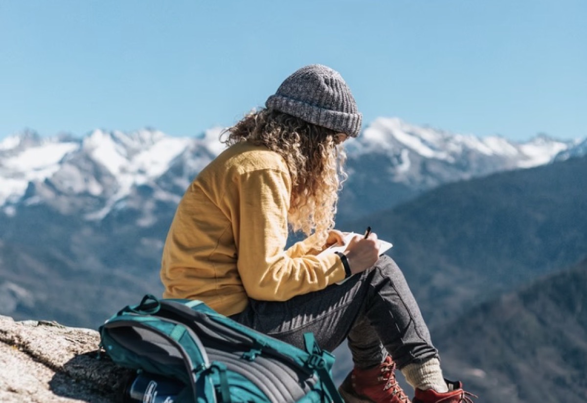 Woman sitting outside in the mountains journaling.
