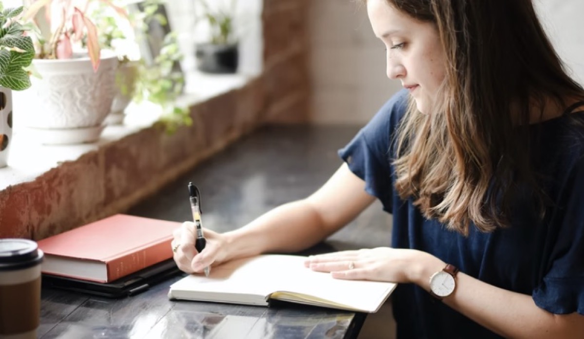 Woman journaling in a coffee shop with plants and a quiet space.