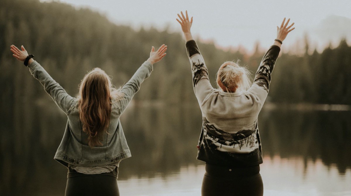 Girls excited and free at a lake in front of the mountains. Unsplash - Priscilla Du Preez