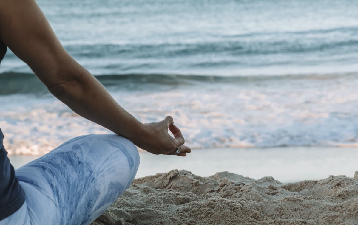 Woman meditating on the beach. Unsplash - Chelsea Gates