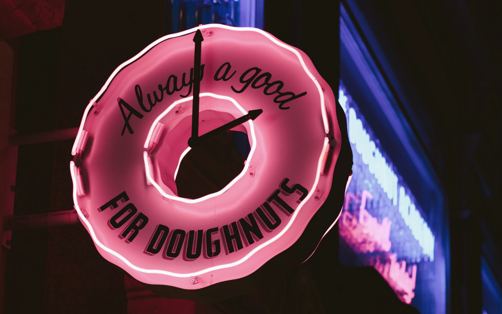 A neon sign of a donut place that says it's always a good time for a doughnuts. 