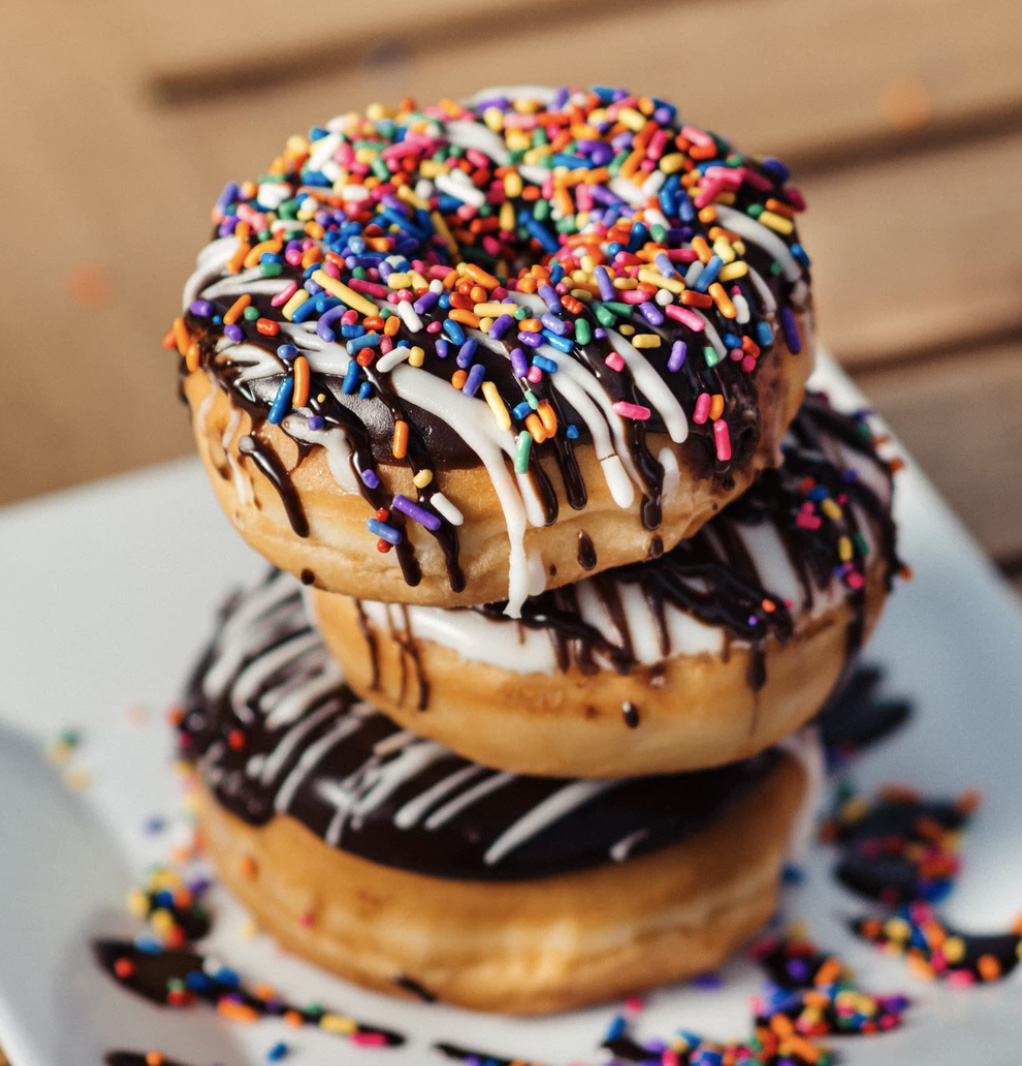 A stack of 3 donuts on top of each other that are chocolate frosted and with sprinkles. 