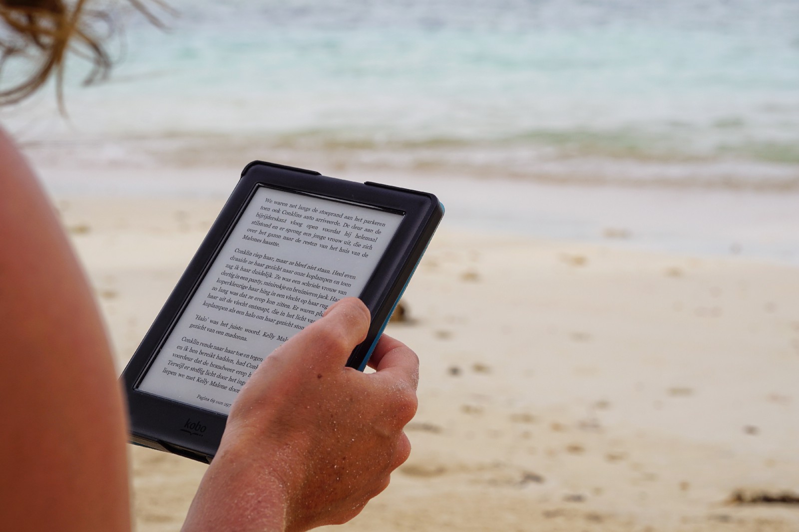A woman on the beach reading a tablet in the sun. 