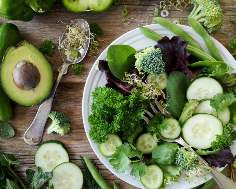 A plate and table full of green vegetables - cucumbers, broccoli, avocado, peas