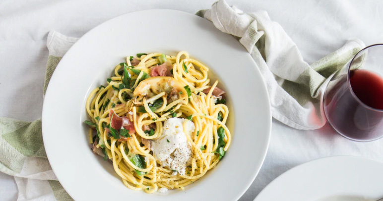 A plate full of pasta with vegetables and a glass of wine