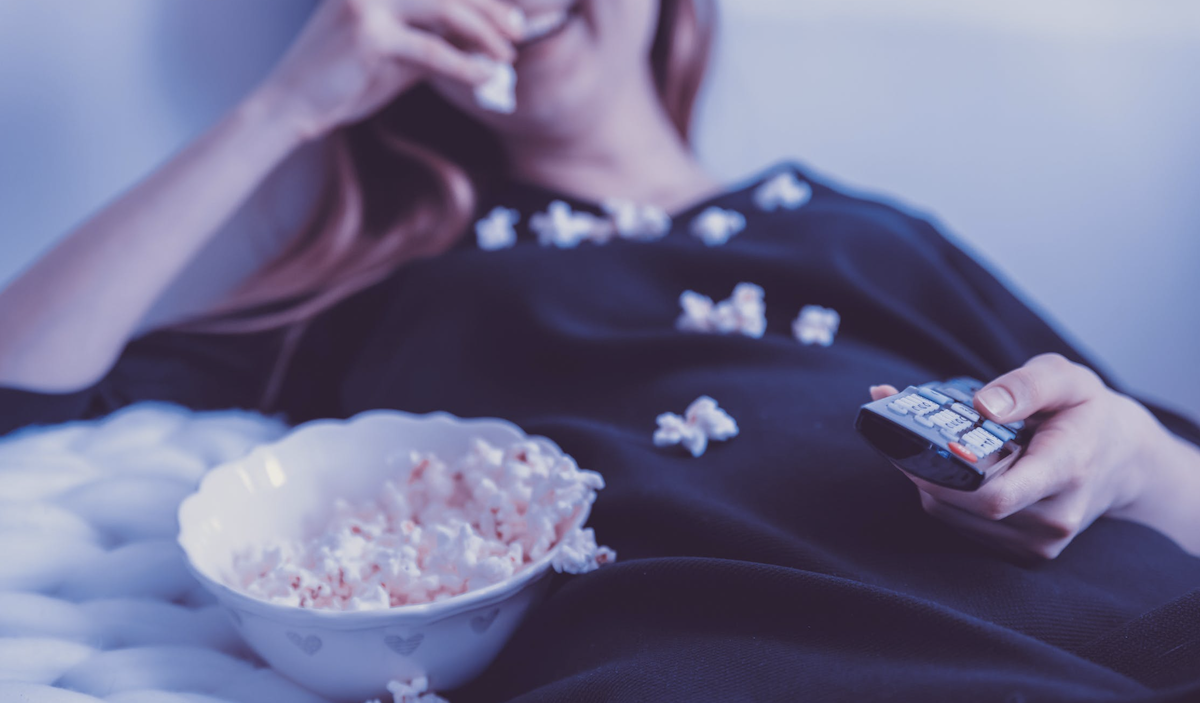 woman eating popcorn in front of TV as a snack