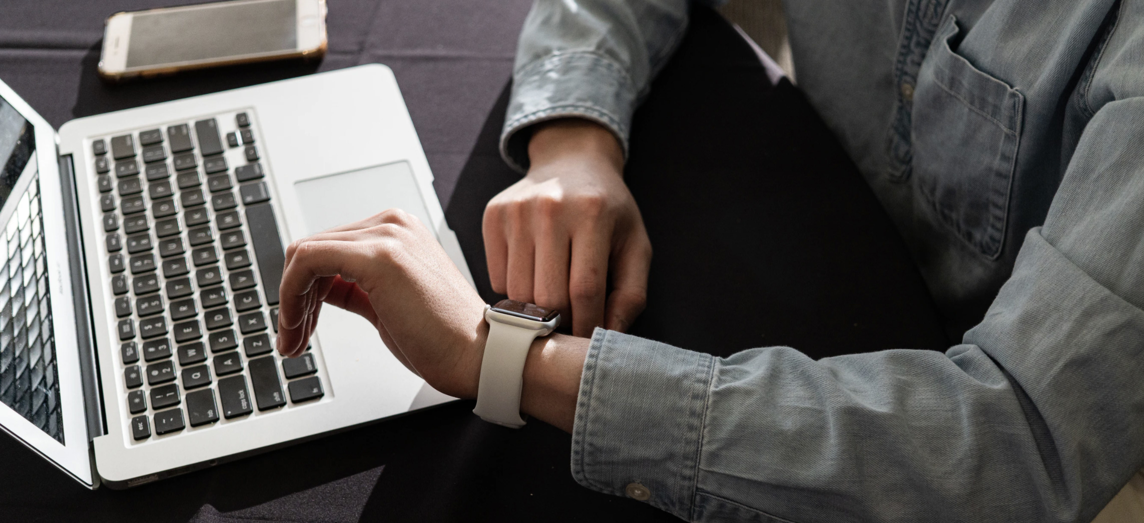 Woman on lap top and checking watch for time