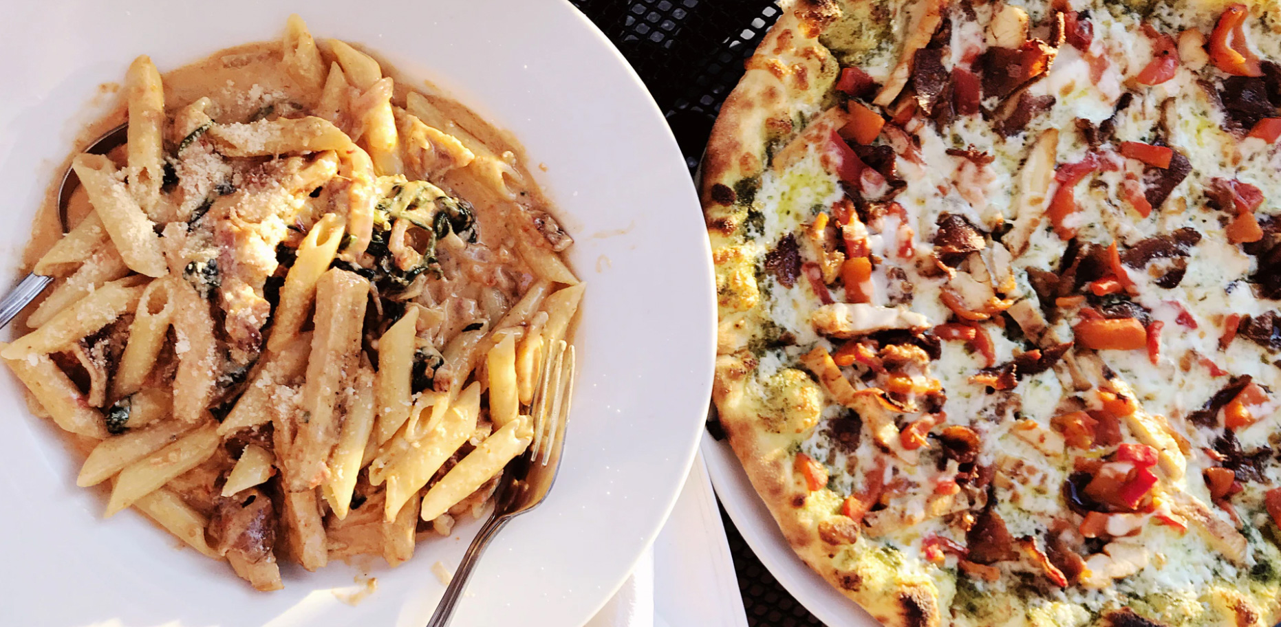 A plate of pasta and a pizza next to each other on a table. 
